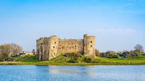 A historic castle with a moat, surrounded by greenery and a clear sky.