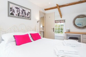 Une chambre à coucher avec un lit, des oreillers, un tableau, un miroir et une fenêtre avec des rideaux.