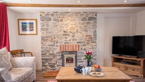 A cozy living room with a stone fireplace, a sofa, a coffee table with a vase of flowers, and a television. - Carew Cottage, Holiday Cottage Carew, Sleeps 4, 2 bedrooms,  bathrooms (Tenby)