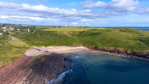 An aerial view of a coastal area with a beach, cliffs, and a small settlement.