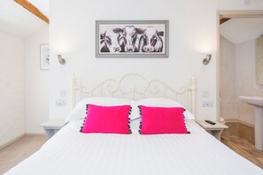 A bed with white bedding and two bright pink pillows, a white metal headboard, a framed picture of cows on the wall, and a bedside table with a remote control. - Carew Cottage, Holiday Cottage Carew, Sleeps 4, 2 bedrooms,  bathrooms (Tenby)