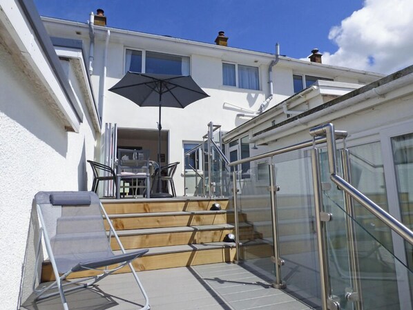 A modern apartment with a glass staircase, a dining area with chairs and a table, and an umbrella.