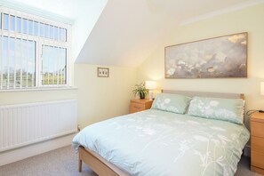 Een slaapkamer met een bed, nachtkastjes, een raam en een schilderij aan de muur.