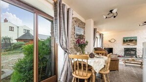 A cozy living room with a stone fireplace, a dining table with chairs, and a large window overlooking a garden. - Coachmans Cottage, Holiday Cottage Nr St Brides, Sleeps 3, 2 bedrooms,  bathrooms (Haverfordwest)