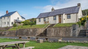 A coastal building with a stone staircase leading to a wooden door, a picnic table in the foreground, and a clear blue sky. - Coastal View, Holiday Cottage Porthgain, Sleeps 4, 2 bedrooms,  bathrooms (Haverfordwest)