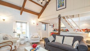 A cozy living room with a grey sofa, white armchair, and a small table with a teapot and pastries. A staircase leads to an upper level with a kitchen visible. - Crab Cottage, Holiday Cottage Aberfforest Beach, Newport, Sleeps 6, 3 bedrooms,  bathrooms (Newport)