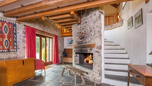 Un interior rústico con chimenea de piedra, vigas de madera y una escalera.