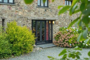 Traditional stone building with a prominent entrance, surrounded by lush greenery and gravelled grounds.