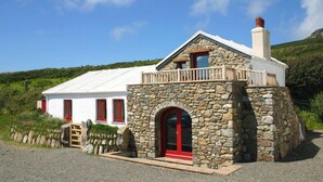Une maison en pierre avec une porte rouge et des murs blancs, un balcon et une cheminée.