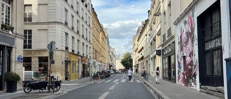 A street view with buildings on both sides, a clear sky, and a few pedestrians.
