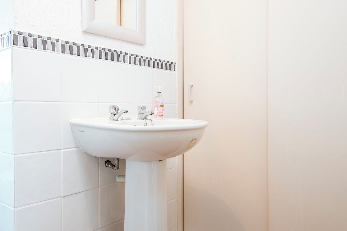 Valkoinen kylpyhuone, jossa on jalkapallipylväsallas, sen yläpuolella peili ja wc-istuin.