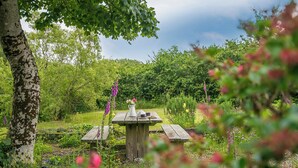A wooden picnic table in a lush garden with a vase of flowers.