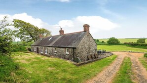 A stone house with a sloped roof, a chimney, and a small porch with chairs. - Felin Fach, Holiday property Llandeloy, Sleeps 8, 4 bedrooms,  bathrooms (Haverfordwest)