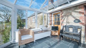 A conservatory with a glass roof, wicker furniture, a stone bench, and a television on a wooden stand. - Felin Fach, Holiday property Llandeloy, Sleeps 8, 4 bedrooms,  bathrooms (Haverfordwest)
