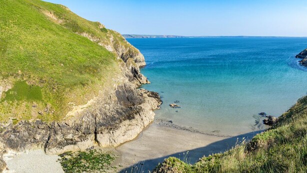 A coastal landscape with a grassy cliff, clear blue sea, and a sandy beach. - Felin Fach, Holiday property Llandeloy, Sleeps 8, 4 bedrooms,  bathrooms (Haverfordwest)
