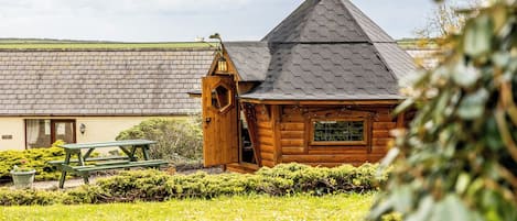 A wooden cabin with a sloped roof and a chimney, surrounded by a well-maintained lawn and a picnic table.