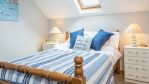 A bedroom with a sloped ceiling, a bed with blue and white striped bedding, two bedside tables with lamps, and a wall with a nautical-themed painting. - Gamekeepers Cottage, Holiday Cottage Nr St Brides, Sleeps 6, 3 bedrooms,  bathrooms (Haverfordwest)