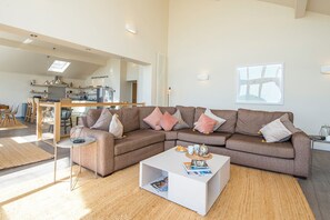 A modern living room with a sectional sofa, a coffee table, and a dining area with chairs and a table. - Genoa, Holiday Home Penally , Sleeps 8, 4 bedrooms,  bathrooms (Tenby)