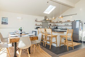 A modern kitchen with a dining area, featuring a central island, pendant lighting, and a view of the city through a skylight. - Genoa, Holiday Home Penally , Sleeps 8, 4 bedrooms,  bathrooms (Tenby)
