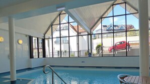 An indoor swimming pool with clear windows, a pool ladder, and a table with chairs.