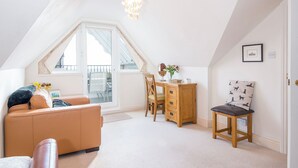 A cozy loft bedroom with a sloped ceiling, a large window, a desk, a chair, and a bed.