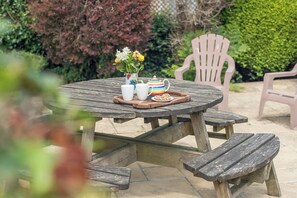 A wooden picnic table with a vase of flowers, two white cups, a teapot, and a tray with cookies. - Glandraeth, Holiday Cottage Newport, Sleeps 4, 2 bedrooms,  bathrooms (Newport)