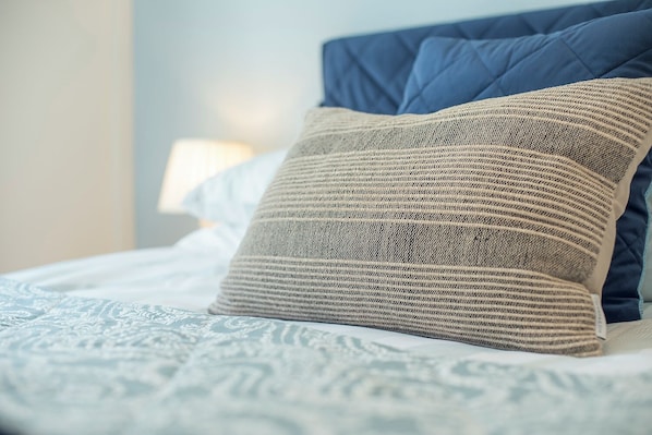 A bed with a patterned bedspread, a blue headboard, and a beige pillow.