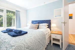 A bedroom with a bed, pillows, a nightstand, a lamp, and a window with curtains. - Glandraeth, Holiday Cottage Newport, Sleeps 4, 2 bedrooms,  bathrooms (Newport)