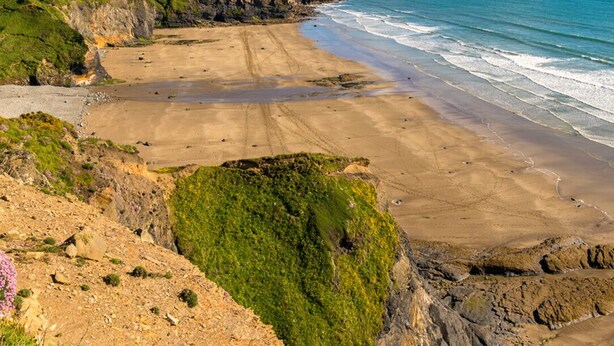 Eine Küstenlandschaft mit Sandstrand, grasbewachsenen Klippen und Blick auf das Meer.