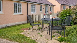 Une terrasse avec une table et des chaises, une bouteille de vin et un vase de fleurs.