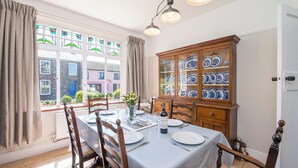 A dining room with a table set for four, a wooden cabinet with blue and white plates, and a bottle of wine on the table. - Gorwel, Holiday Home St Davids, Sleeps 6, 3 bedrooms,  bathrooms (Haverfordwest)