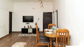 A dining area with a wooden table, chairs, and a television mounted on the wall. - Kodaikanal Misty Family Resort (Kodaikanal)