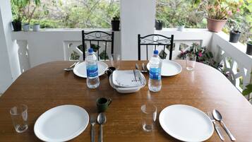 A dining table set with plates, cutlery, and water bottles, surrounded by potted plants.