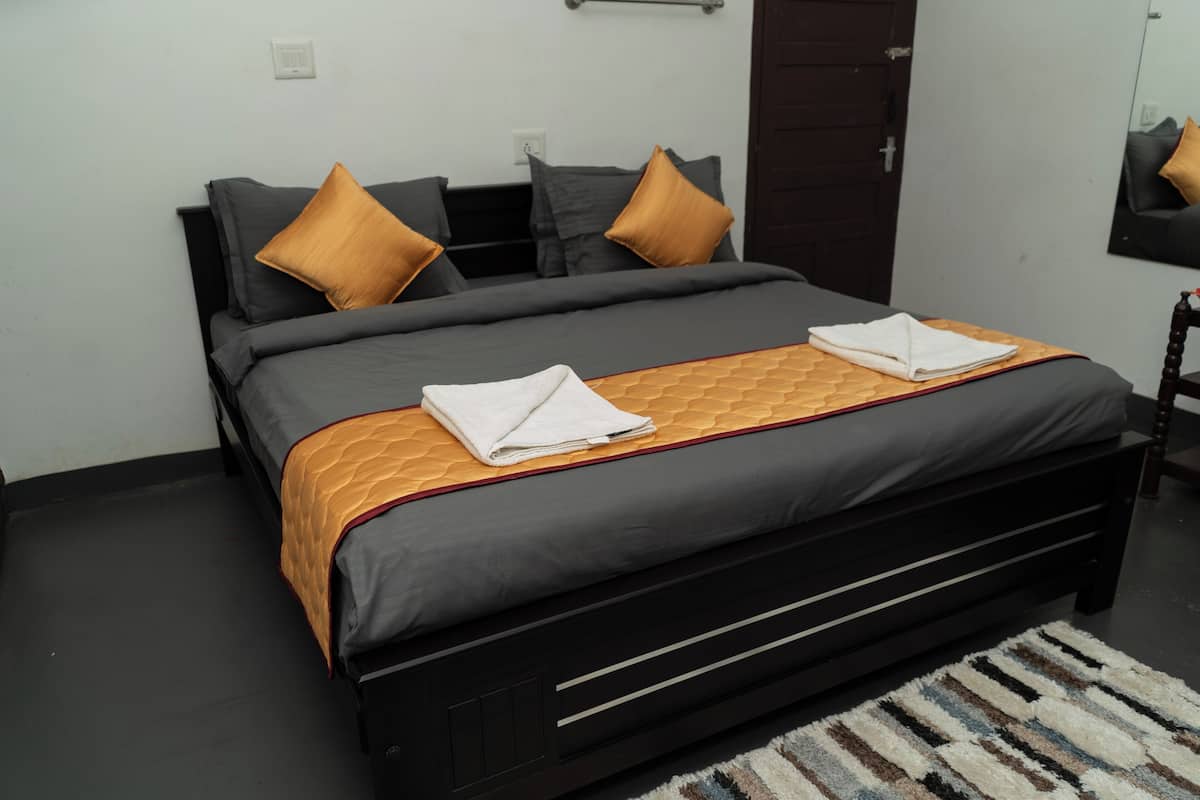 A neatly made bed with a grey and orange bedspread, two pillows, and two folded towels.