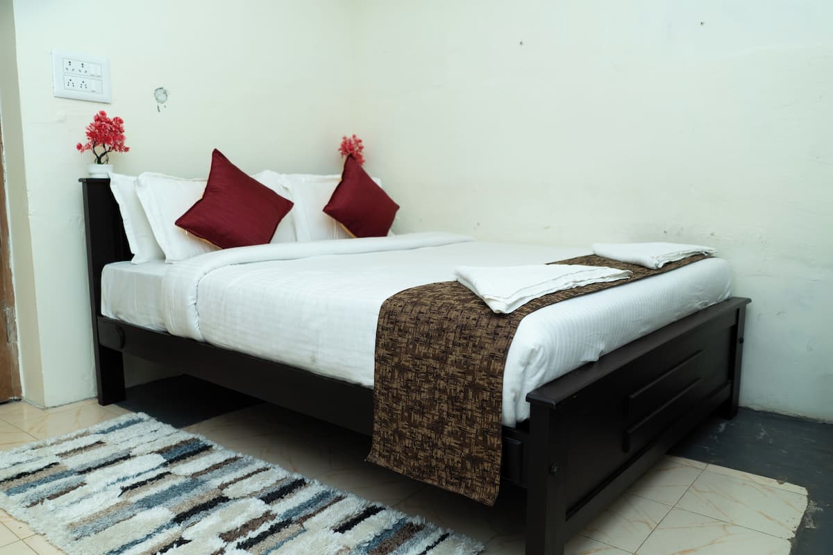 A neatly made bed with white bedding and a brown throw, a dark wooden headboard, and a striped rug on a tiled floor.