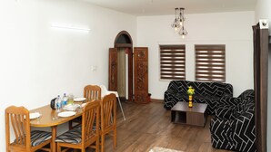 A dining area with a wooden table and chairs, a sofa, and a small coffee table with a vase. - Kodaikanal Misty Family Resort (Kodaikanal)