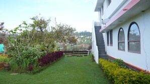 A modern building with a white exterior and red accents, a well-maintained garden with various plants, and a clear view of the surrounding area. - Kodaikanal Misty Family Resort (Kodaikanal)