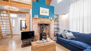 A cozy living room with a brick fireplace, a blue couch, a wooden coffee table, and a TV.