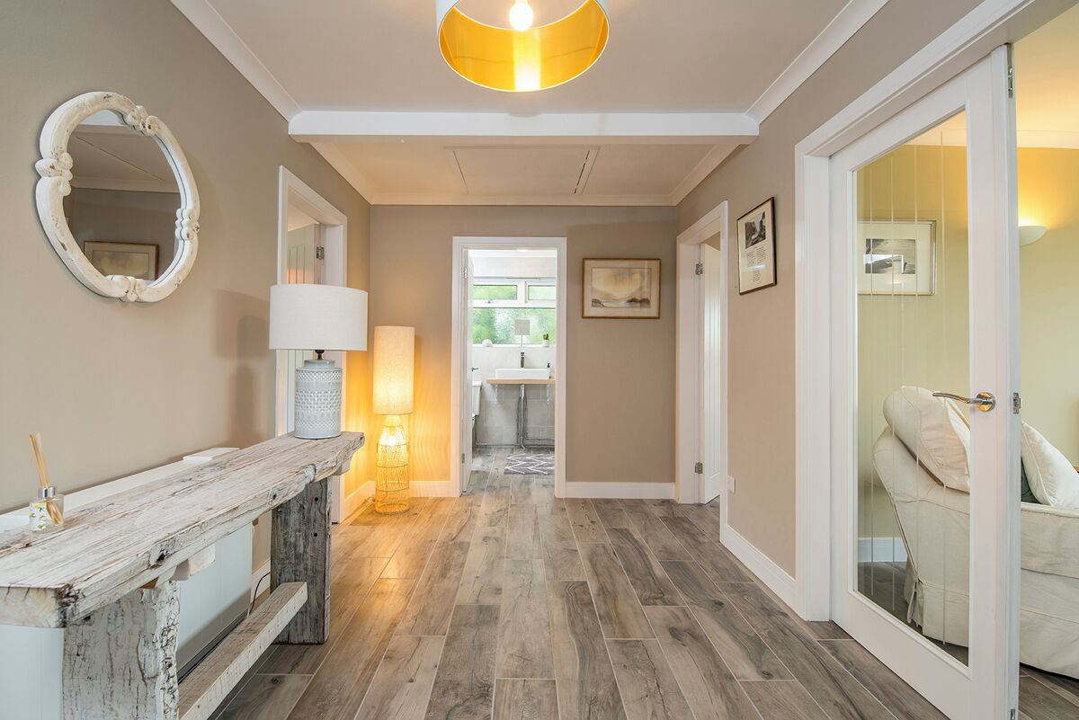 A hallway with a rustic wooden bench, a mirror, a lamp, and a door leading to a bathroom.