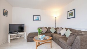 A living room with a flat-screen TV on a white stand, a brown sofa set with cushions, a wooden coffee table with a vase and cups, and a floor lamp. - Hafod, Holiday Home Broad Haven, Sleeps 4, 2 bedrooms,  bathrooms (Broad Haven)