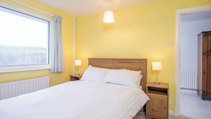 A bedroom with a bed, two bedside tables with lamps, a window with curtains, and a radiator. - Hafod, Holiday Home Broad Haven, Sleeps 4, 2 bedrooms,  bathrooms (Broad Haven)