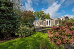 A modern building with a covered outdoor area, surrounded by lush greenery and a well-maintained lawn.