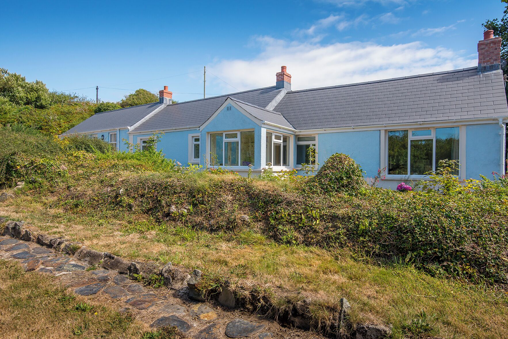 A coastal house with a grey tiled roof, white-framed windows, and a brick chimney.