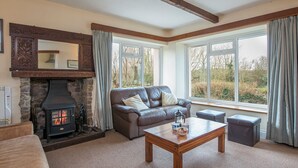 A cozy living room with a stone fireplace, leather sofa, and large windows offering a view of the outdoors. - Halfways, Holiday Home St Davids, Sleeps 8, 4 bedrooms,  bathrooms (HAVERFORDWEST)