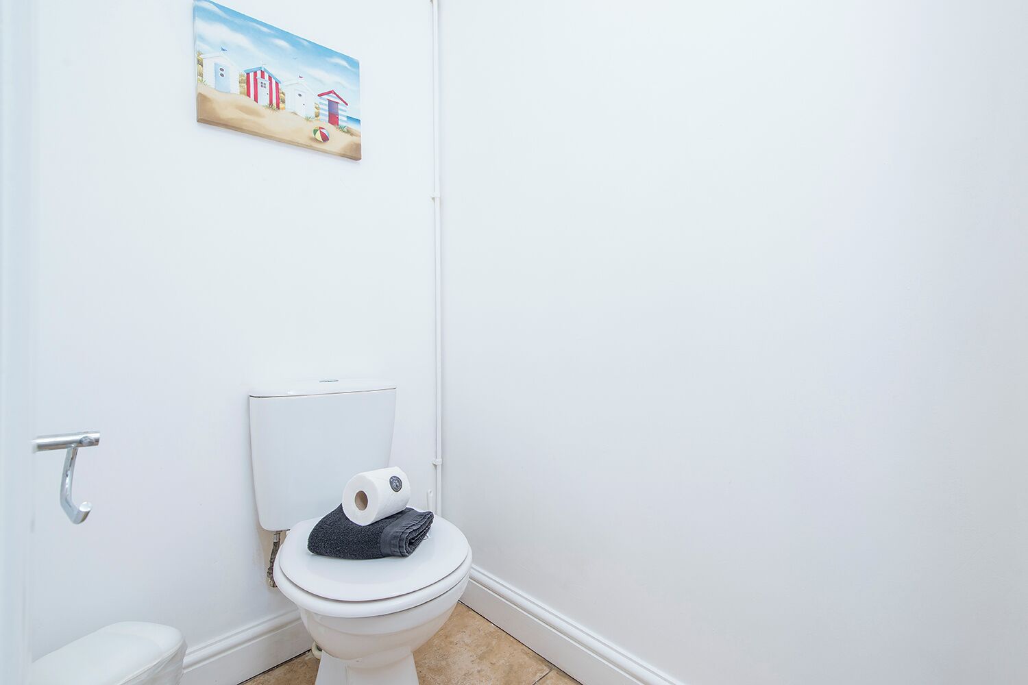 A bathroom with a toilet, a roll of toilet paper, and a painting of a beach scene on the wall.
