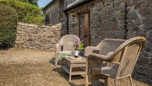 An outdoor seating area with wicker chairs and a table, a stone building with a door, and a gravel ground. - Heather Cottage, Holiday Home Near Nolton Haven, Sleeps 2, 1 bedrooms,  bathrooms (Portfield Gate)