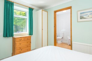 A bedroom with a wooden dresser, a bed, a window with curtains, and a view of a bathroom. - Heddfan Cottage, Holiday Home Little Haven, Sleeps 4, 2 bedrooms,  bathrooms (Haverfordwest)