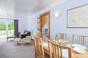 A dining area with a wooden table set for four, a sofa, and a bookshelf in the background. - Heddfan Cottage, Holiday Home Little Haven, Sleeps 4, 2 bedrooms,  bathrooms (Haverfordwest)
