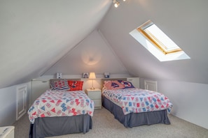 Une chambre avec deux lits, une lucarne et une table de chevet avec une lampe.