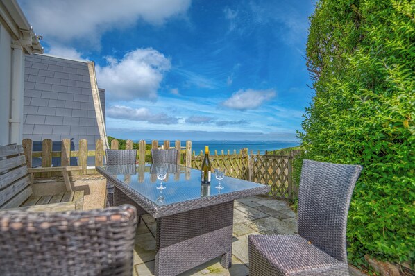 An outdoor patio with wicker furniture, a glass table, and a view of the sea. - Heddfan Cottage, Holiday Home Little Haven, Sleeps 4, 2 bedrooms,  bathrooms (Haverfordwest)